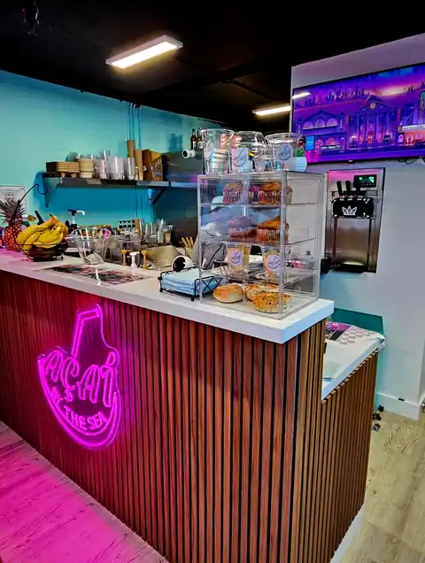 Inside the shop — neon Açaí By The Sea sign at the counter